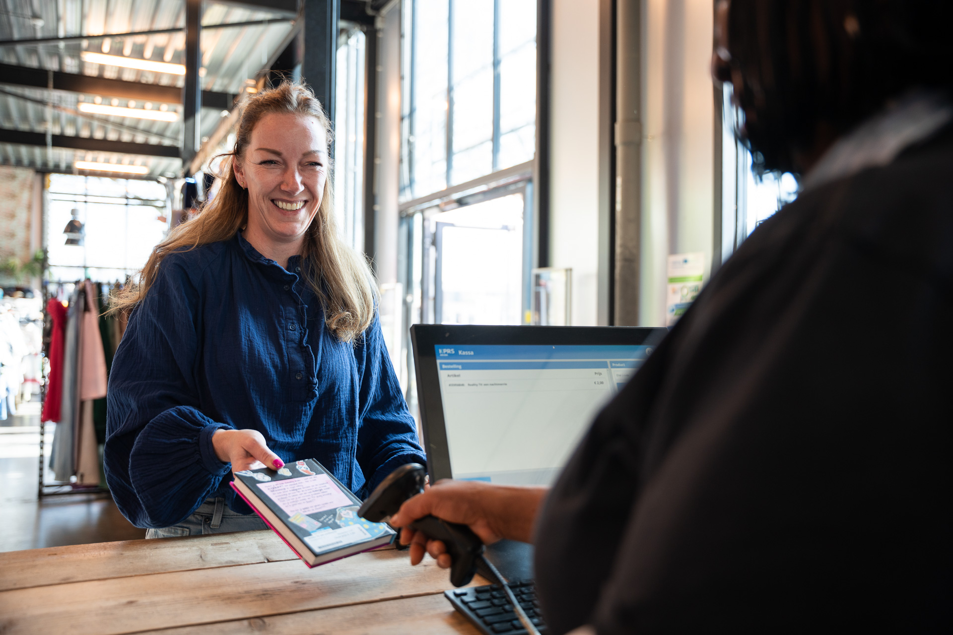 Kringloopmedewerker scant een boek met de KPRS Kassa. De klant lacht en is blij.