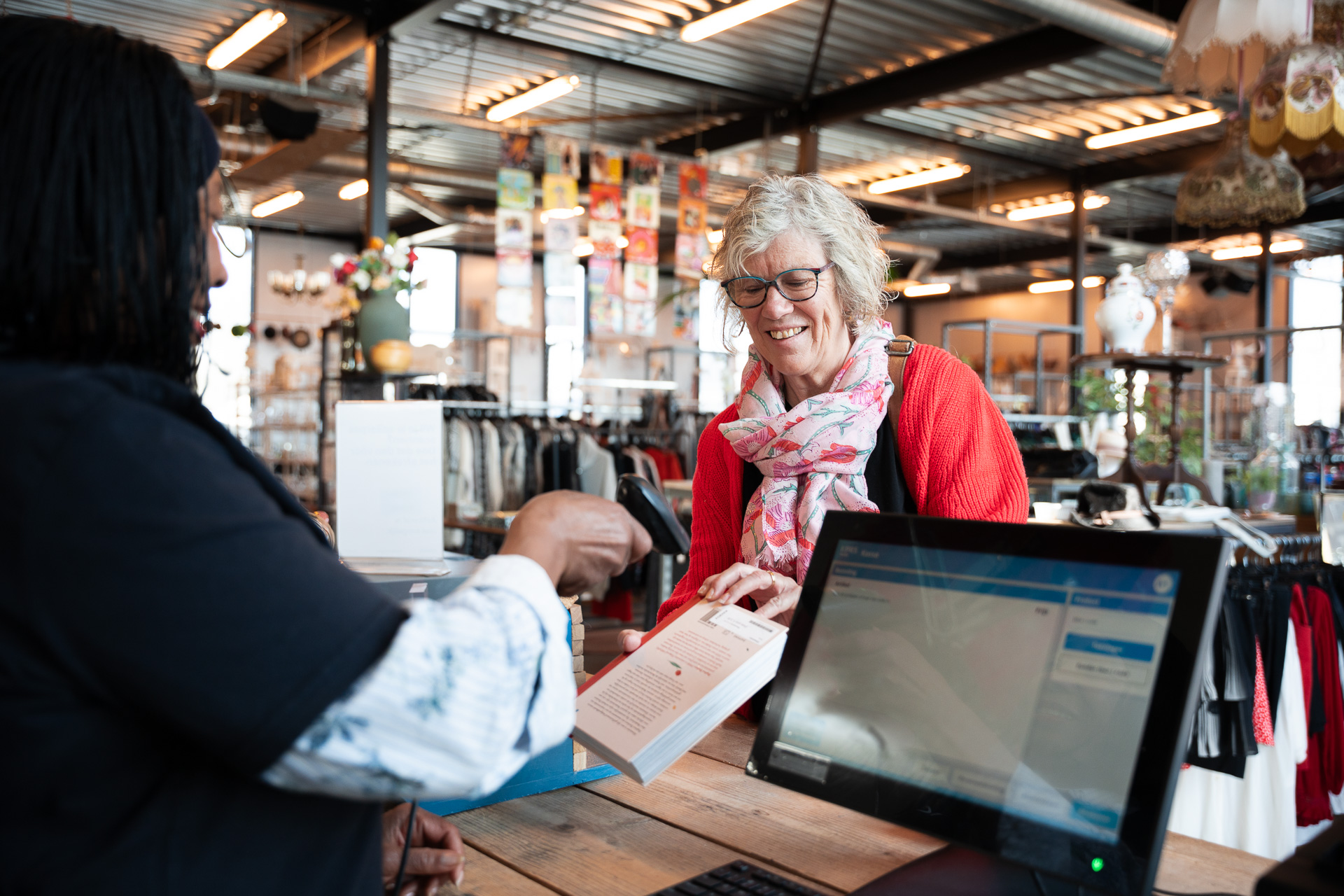 Kringloopmedewerker scant een boek met de KPRS Kassa. De klant lacht en is blij.